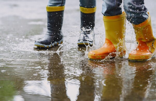 criancas_engracadas_em_botas_de_chuva_brincando_com_navio_de_papel_por_uma_poca