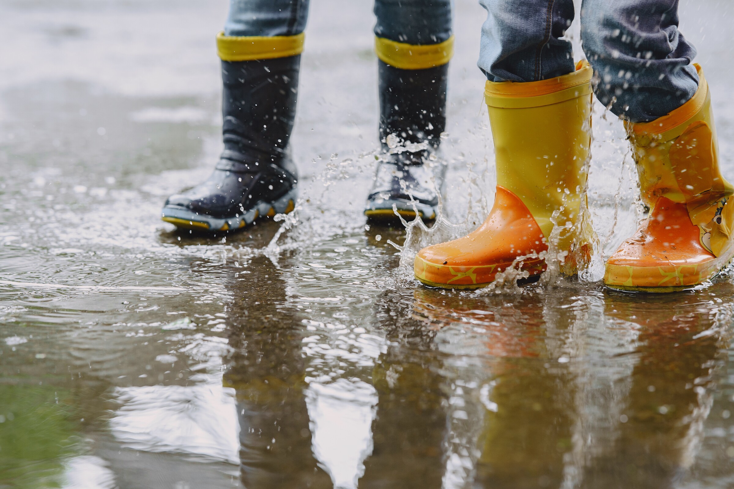 criancas_engracadas_em_botas_de_chuva_brincando_com_navio_de_papel_por_uma_poca
